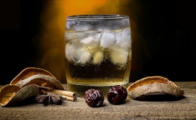 Kräutersaft und Obst in einem Glas gefüllt mit Eis und getrockneten Früchten und getrockneten Kräutern auf einem alten Holztisch auf unscharfem Bokeh-Hintergrund.