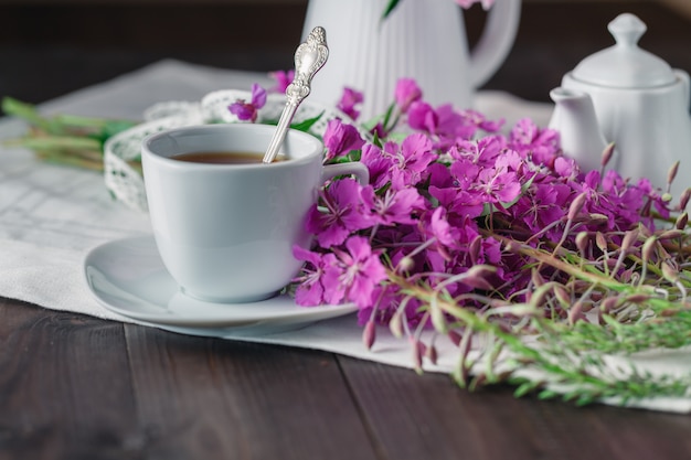 Kräutertee in einer Glasschale, frische Blumen Weidenröschen gegen das dunkle Holzbrett