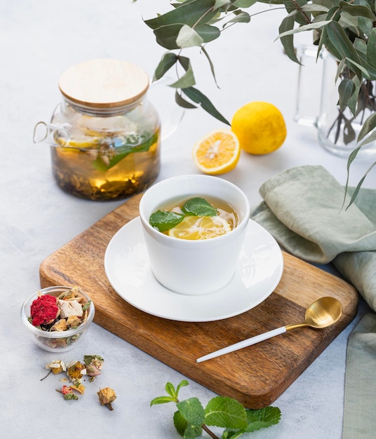 Kräutertee mit Zitrone und Minze in einer weißen Tasse auf einem Holzteller auf hellem Hintergrund mit Eukalyptuszweigen und einer Teekanne das Konzept eines gesunden und köstlichen Getränks für die Immunität