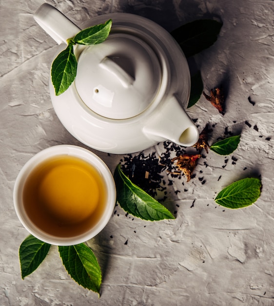 Kräutertee, Tassen und Teekanne mit Blättern auf grauem Betonhintergrund.