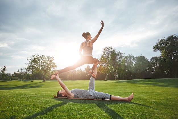 Kraft und Flexibilität junges und gesundes Paar, das Acro-Yoga in der Natur an einem sonnigen Ort macht