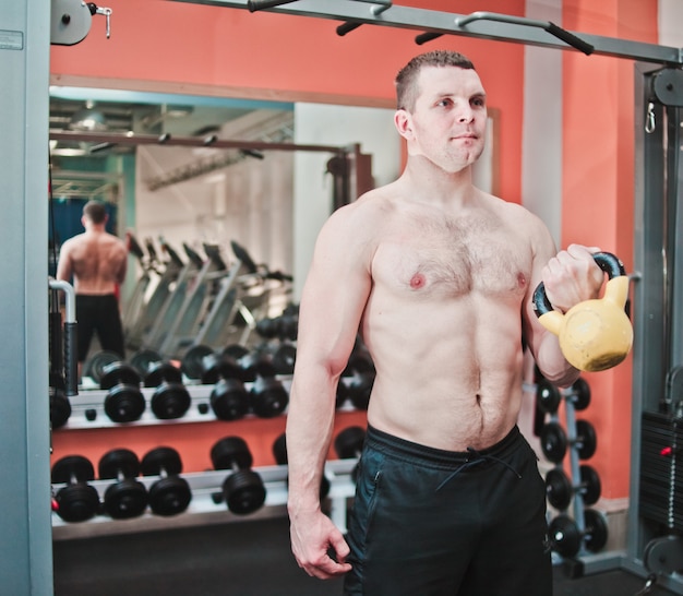 Kraftvoll und stark. Athletischer Mann mit nacktem Oberkörper, der Übungen mit Kettlebell im Fitnessstudio macht