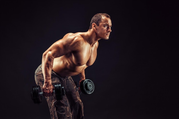 Kraftvoller Mann macht Übungen mit Hanteln. Foto eines jungen Mannes mit gutem Körperbau, isoliert auf schwarzem Hintergrund