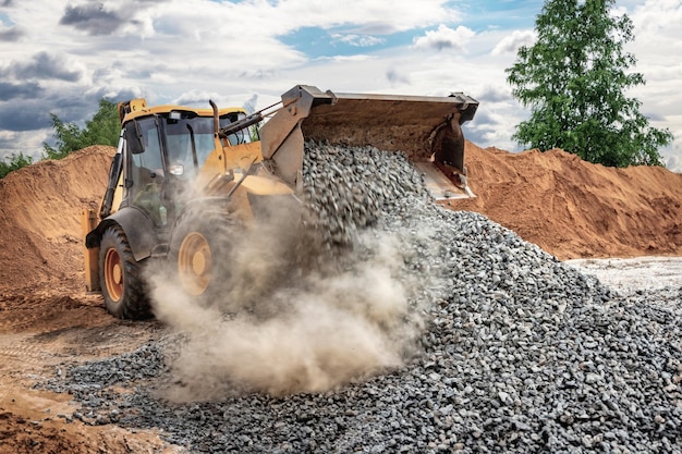 Kraftvoller Radlader oder Bulldozer auf dem Himmel Hintergrund Lader gießt zerquetschten Stein oder Kies