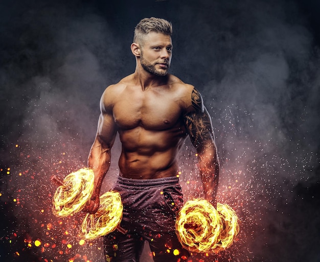 Kraftvoller, stylischer Bodybuilder mit Tätowierung auf dem Arm, der die Übungen mit Hanteln macht. Konzept der Feuerkunst.