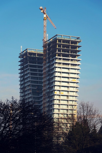 Kran auf Wolkenkratzerbaustelle mit Fenstern, die den Himmel reflektieren