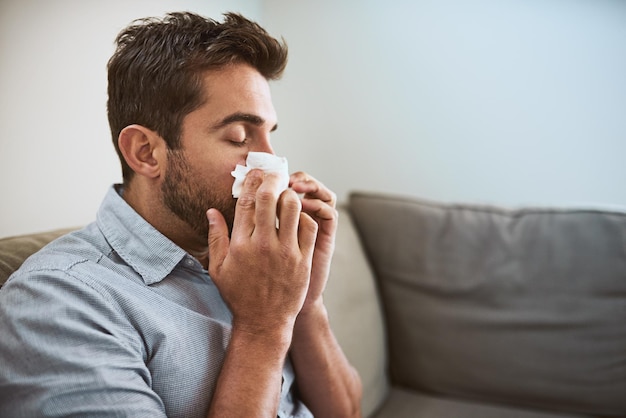 Krank zu Hause und Mann mit Gewebe Blasen der Nase für Allergien Heuschnupfen und Virusinfektion Gesundheitsversorgung Allergie Problem und Person auf dem Sofa mit Krankheit Grippe Symptome und Sinusitis im Wohnzimmer