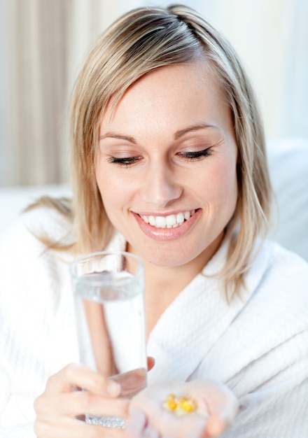 Kranke blonde Frau, die ein Glas Wasser und Pillen hält