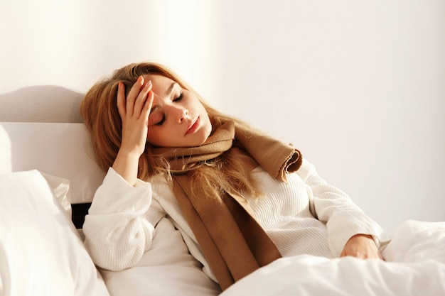 Kranke blonde Frau liegt mit einem Schal im Bett