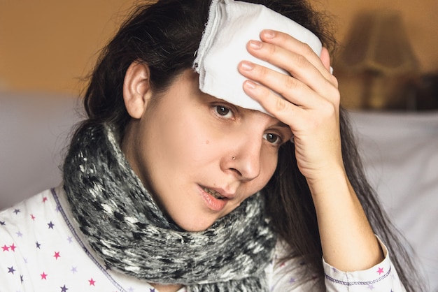 Foto kranke frau erkältet und fieber oder kopfschmerzen bett zu hause. tragen sie den verband nass auf den kopf auf