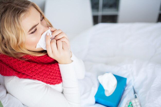 Kranke Frau, Frau mit Grippevirus im Bett liegend, misst sie ihre Temperatur mit einem Thermometer