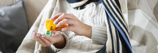 Kranke Frau gießt Tablettenstapel auf die Handfläche und fühlt sich unwohl, wenn sie zu Hause auf der Couch ruht