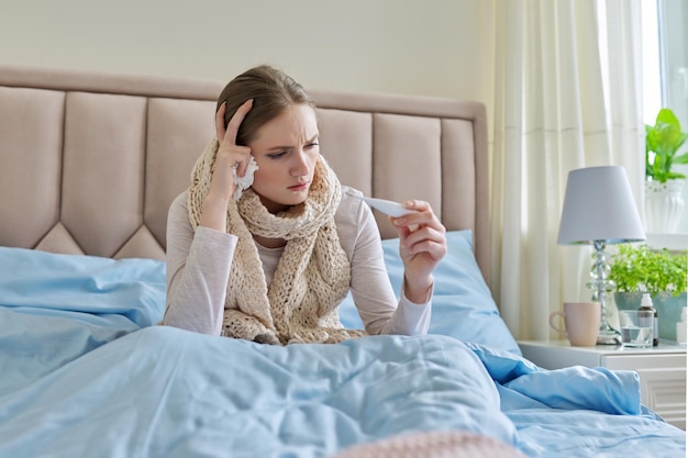 Kranke junge Frau mit Händen, die zu Hause auf dem Bett sitzen