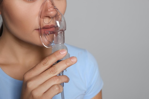 Foto kranke junge frau mit vernebler auf grauem hintergrund nahaufnahme platz für text