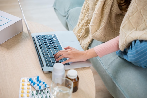 Kranke junge Frau sitzt auf dem Sofa, telefoniert mit dem Laptop online, konsultiert den Arzt zu Hause