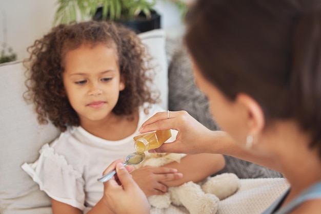 Kranke Tochter, die Medikamente als Heilmittel oder Heilmittel einnimmt, während sie zu Hause auf dem Sofa für Gesundheit und Genesung liegt Krankes Mädchen, das von ihrer liebevollen und fürsorglichen Mutter Medikamente mit einem Löffel verabreicht bekommt