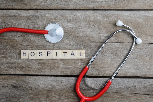 Krankenhaustextwort gemacht mit hölzernen Blöcken und rotem Herzen, Stethoskop auf Holztisch