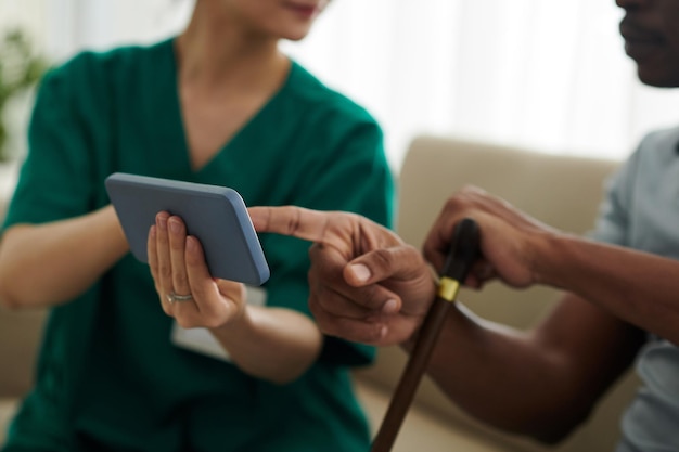 Krankenpflegerin besucht den Patienten zu Hause und zeigt ihm die Telemedizin-Anwendung auf dem Smartphone