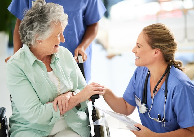 Krankenschwester bespricht Behandlungen mit ihrer rollstuhlgebundenen älteren Patientin im Krankenhaus