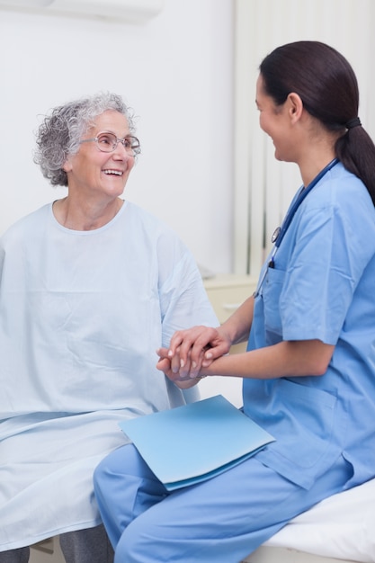 Krankenschwester, die auf Bett mit einem Patienten sitzt