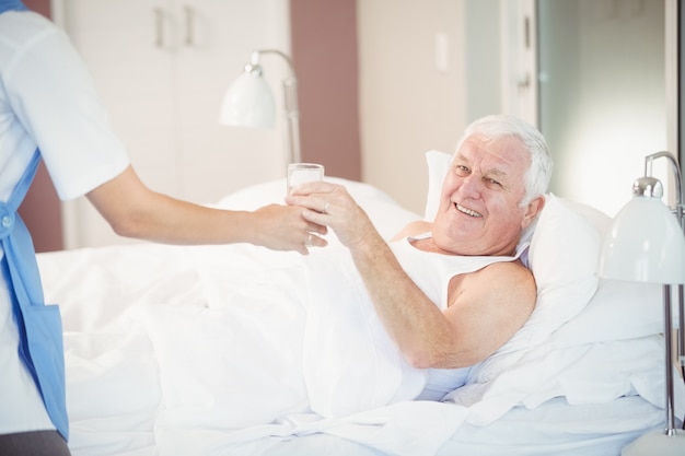 Krankenschwester, die dem älteren Mann Wasserglas gibt