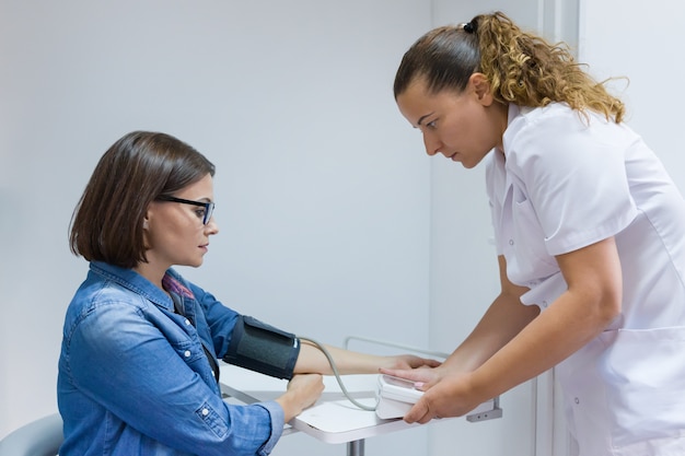 Krankenschwester, die den Blutdruck des weiblichen Patienten im Büro nimmt