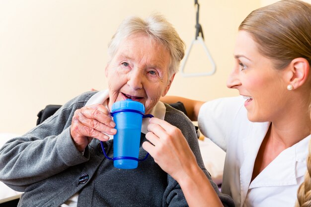 Krankenschwester, die der älteren Frau im Rollstuhl Getränk gibt