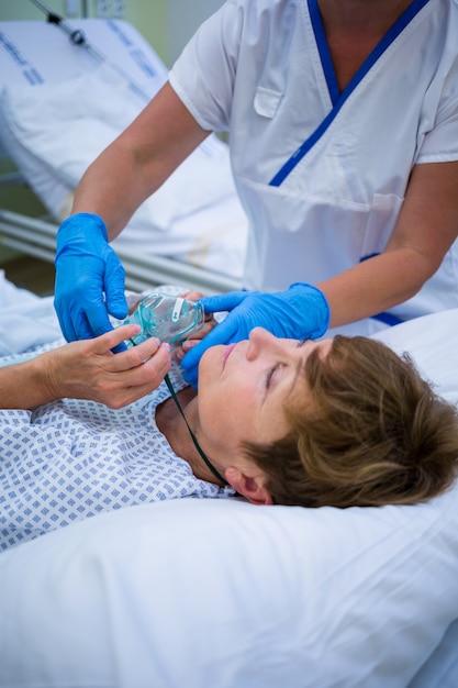 Krankenschwester, die eine Sauerstoffmaske auf das Gesicht eines Patienten setzt