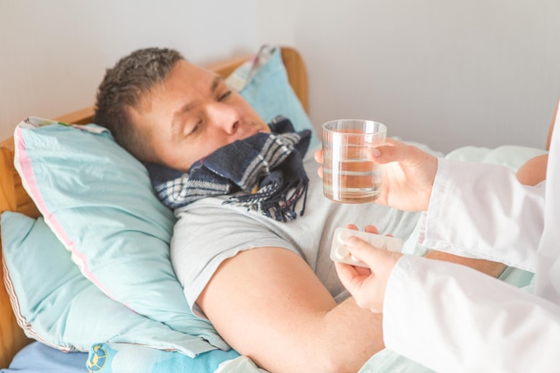 Krankenschwester, die einem männlichen Patienten, der auf einem Krankenhausbett liegt, Pillen und Glas mit Wasser gibt