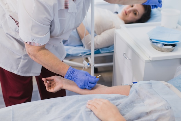 Krankenschwester, die im Krankenhausbett einen intravenösen Schlauch an der Hand des Patienten anbringt