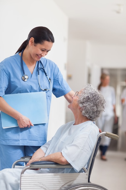 Krankenschwester, die nahe bei einem Patienten in einem Rollstuhl steht