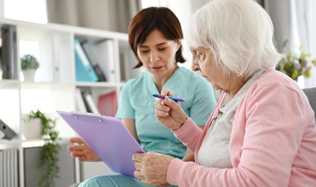 Krankenschwester hilft einer älteren Frau bei der Unterzeichnung von Dokumenten im Pflegeheim