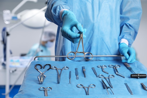 Krankenschwester in der Nähe des Tisches mit verschiedenen chirurgischen Instrumenten im Operationssaal in Nahaufnahme