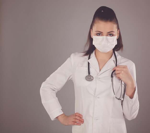 Krankenschwester in Gaze und weißer Robe ist vor grauem Hintergrund mit Stethoskop