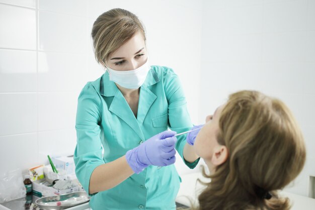 Krankenschwester in medizinischer Maske, die einen Tupfertest auf Coronavirus aus der Nase des Patienten durchführt