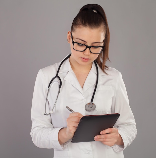 Krankenschwester in weißem Gewand und mit schwarzer Brille schreibt etwas in ihre Notizen dagegen