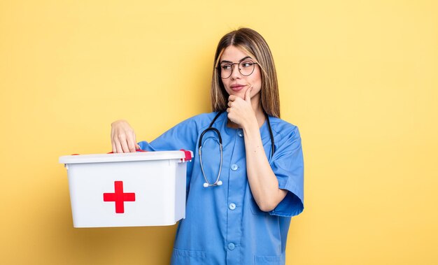 Krankenschwester lächelnd mit einem glücklichen, selbstbewussten Ausdruck mit der Hand am Kinn. Erste-Hilfe-Kit-Konzept