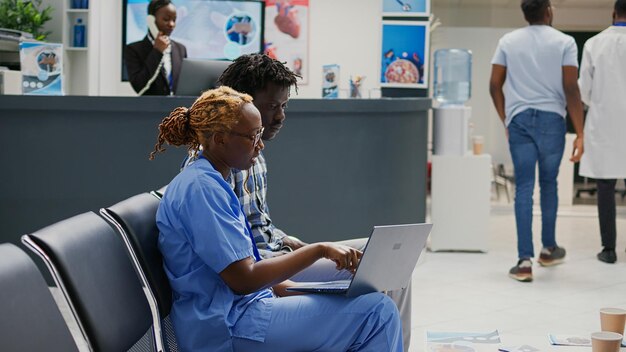 Krankenschwester mit drahtlosem Laptop, um dem Mann die medizinische Behandlung zu zeigen und Krankheiten im Wartebereich zu erklären. Spezialist im Gespräch mit männlichen Patienten über Medicare und Krankheit, Krankenversicherung.