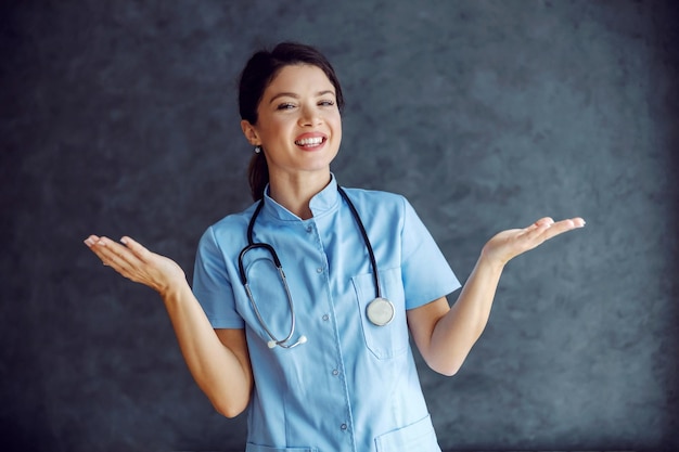 Krankenschwester mit einem Lächeln, das vor grauem Hintergrund steht und die Hände in der Luft hält