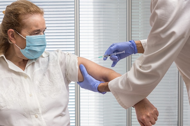 Krankenschwester mit einer Spritze, die den Arm einer älteren Frau mit einer zu impfenden Maske hält