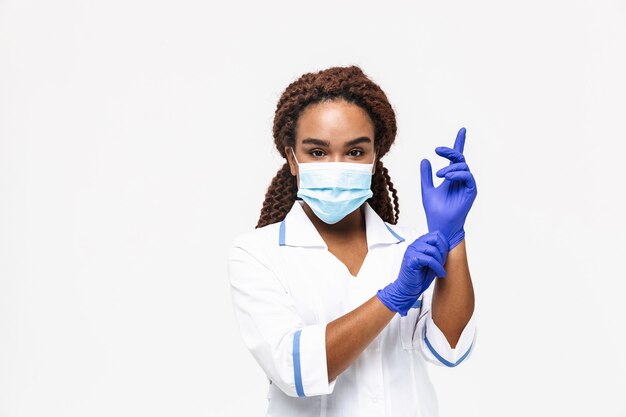 Krankenschwester mit medizinischer Gesichtsmaske mit Einweghandschuhen isoliert gegen weiße Wand