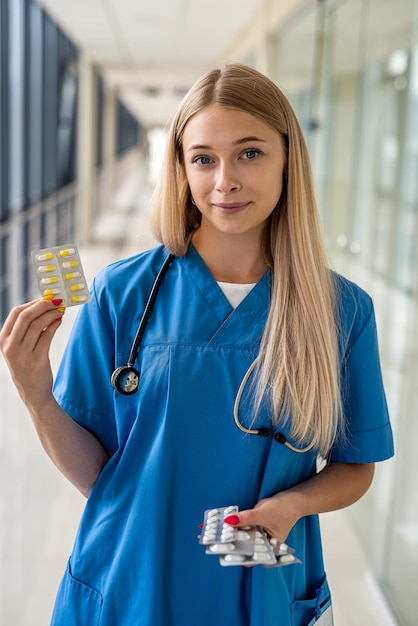 Krankenschwester mit Stethoskop um den Hals, die im Krankenhauskorridor eine Pille in den Händen hält