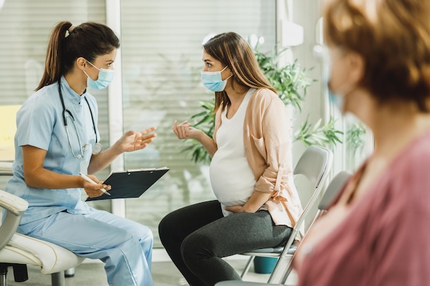 Krankenschwester spricht mit jungen schwangeren Frauen, bevor der Gynäkologe im Wartezimmer des Krankenhauses nachschaut.