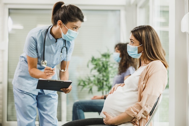 Krankenschwester spricht mit junger schwangerer Frau und macht sich Notizen vor der Kovid-19-Impfung im Wartezimmer des Krankenhauses.