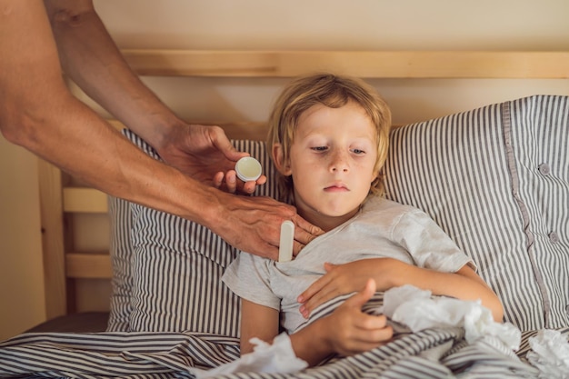 Kranker Junge mit Thermometer im Bett und Vater Hand Temperatur messen Vater überprüft die Temperatur ihres kranken Sohnes, der Thermometer hat Krankes Kind mit Fieber und Krankheit im Bett