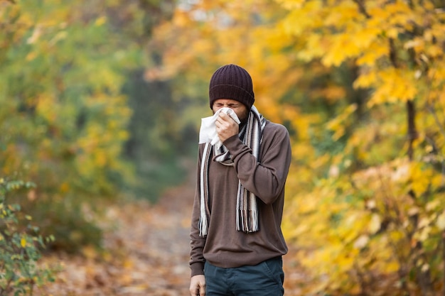 Kranker Mann bläst sich an einem Herbsttag die Nase.