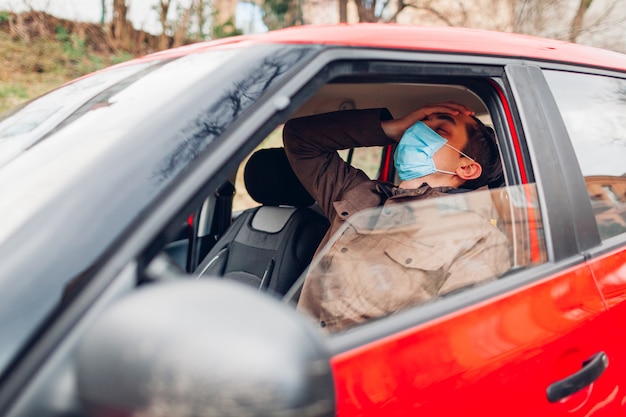 Kranker Mann, der im Auto sitzt und Schutzmaske trägt, fühlt sich fieberkrank, hat Grippe-Covid-19-Coronavirus.