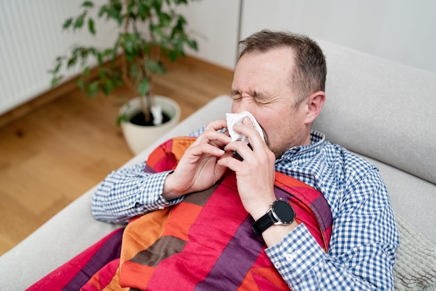 Kranker Mann, der sich die Nase weht, liegt auf dem Sofa Mann mit einer Grippe, die sich so schlecht fühlt