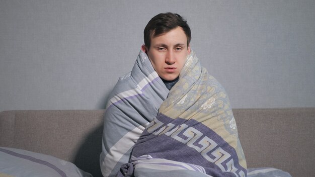 Kranker Mann, der sich in eine warme Decke einwickelt und vor Kälte zittert.