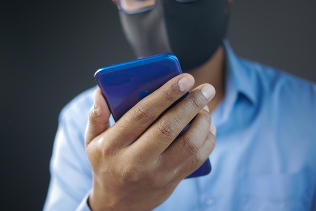 Kranker Mann in chirurgischer Gesichtsmaske mit selektivem Fokus des Smartphones